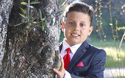 Niño de Comunión con corbata roja semiescondido detrás de un árbol